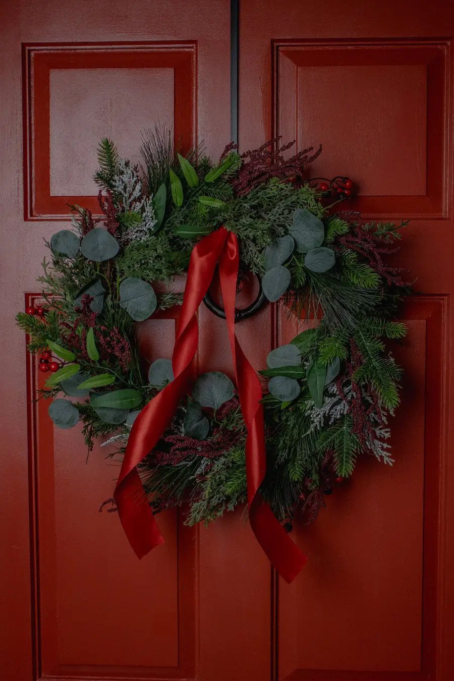 Couronne de Noël avec branches de sapin, d'eucalyptus, et ruban rouge accrochée à une porte rouge