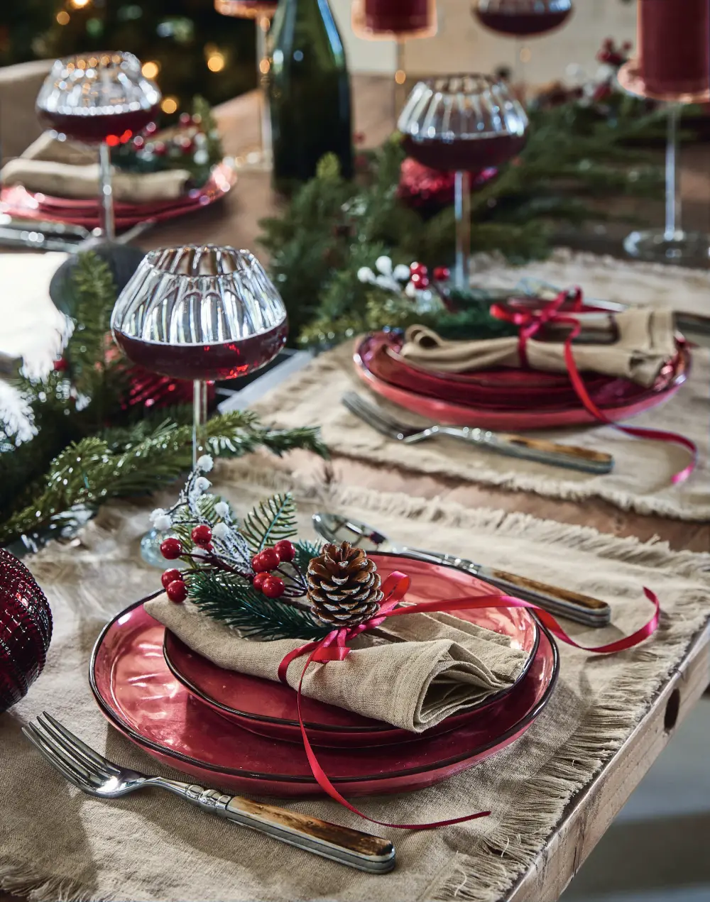 Décoration de table de Noël thème traditionnelle et écoresponsable avec des éléments naturels comme des pommes de pin, des branches de sapins et des baies dans les tons rouges, verts, beiges