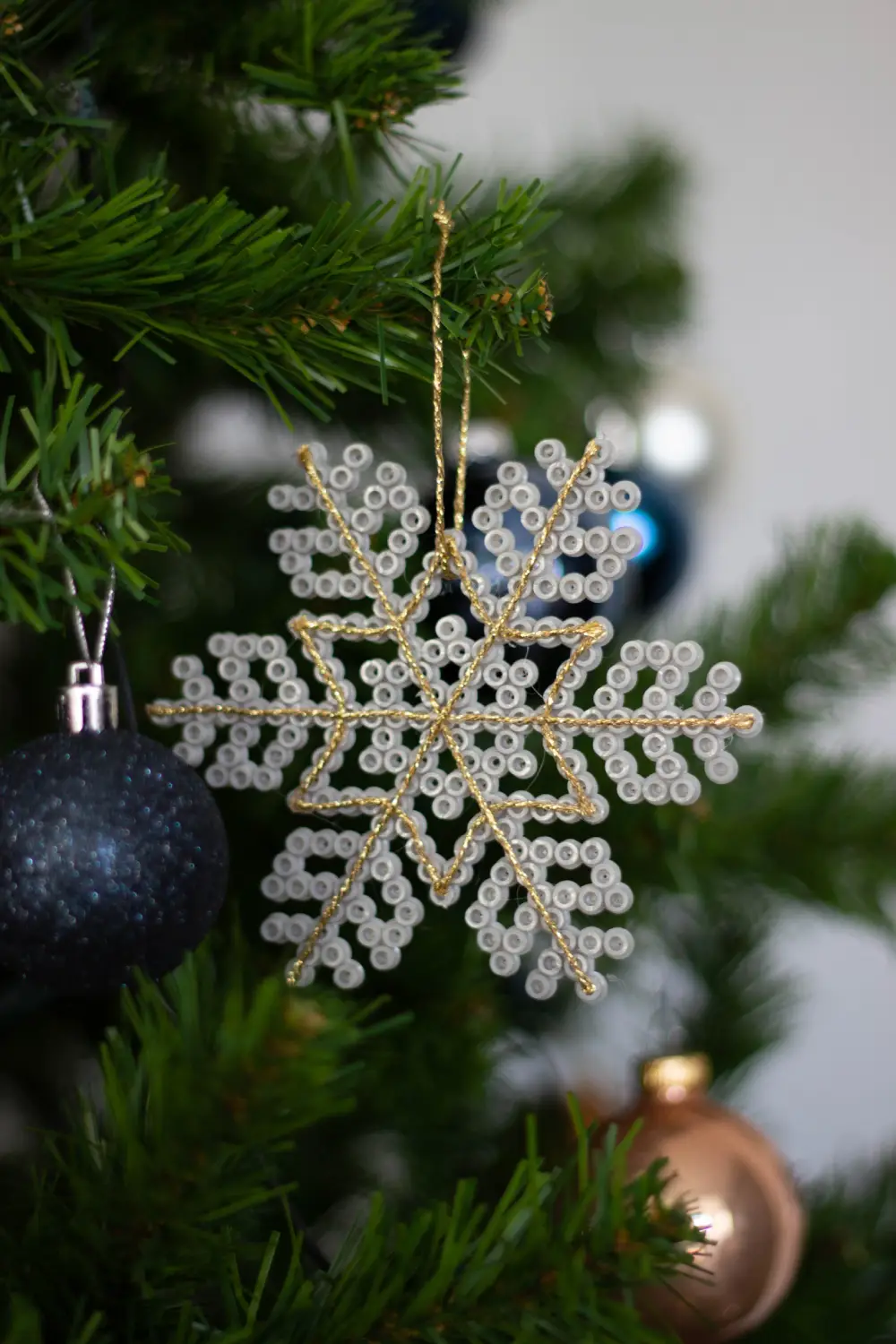 Flocon de neige en perles à repasser gris et fil doré accroché dans le sapin