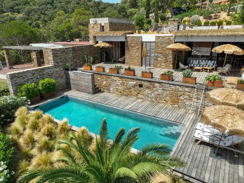 Piscine rectangulaire tout en longueur avec terrasse bois et mur en pierre